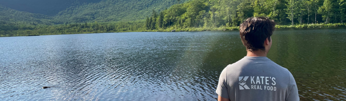 man in Kate's Real Food Shirt overlooking lake